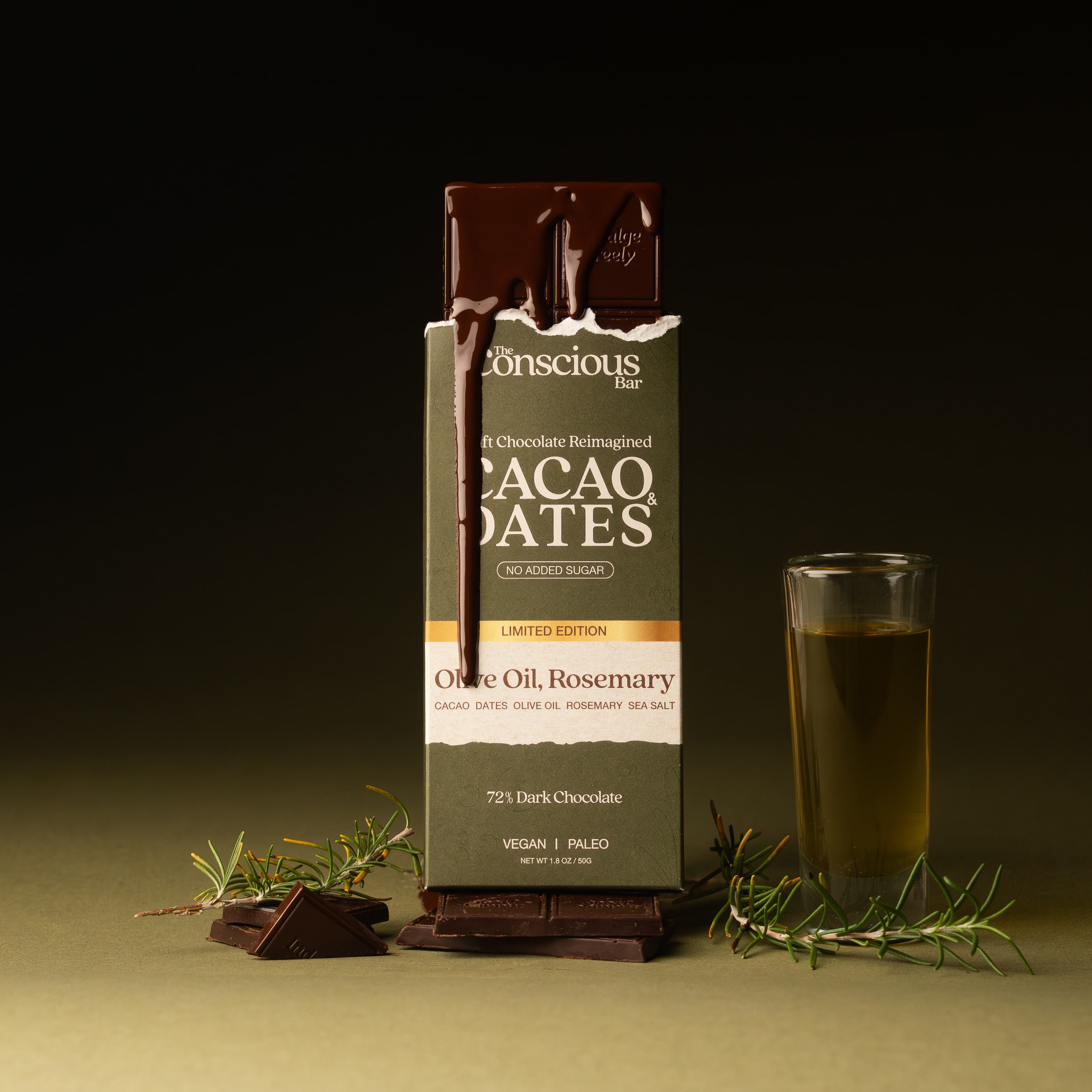 Conscious Bar Cacao Dates chocolate bar with a glass of olive oil and rosemary on a dark background